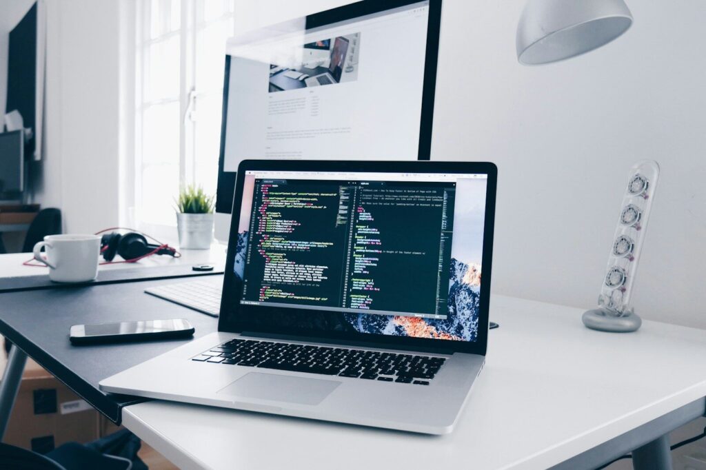 Un MacBook avec des lignes de code affichées à l'écran, posé sur un bureau encombré.